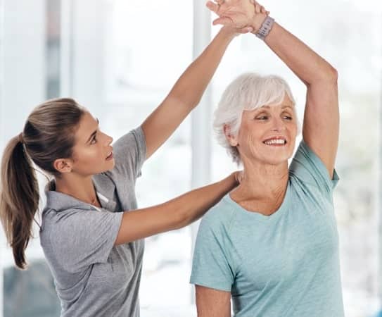 An elderly lady stretching her arms with the help of an chriospot expert