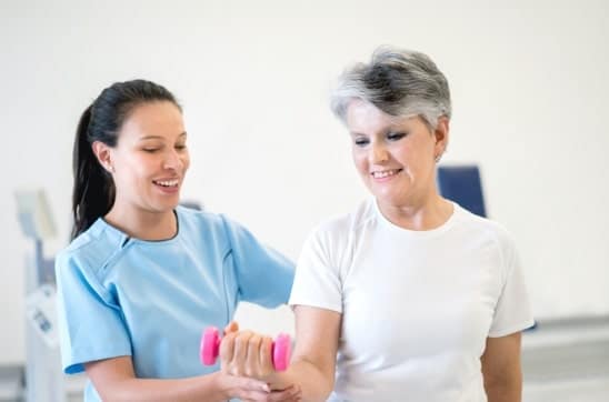 An elderly woman getting assistance in doing bicep curls as physical therapy