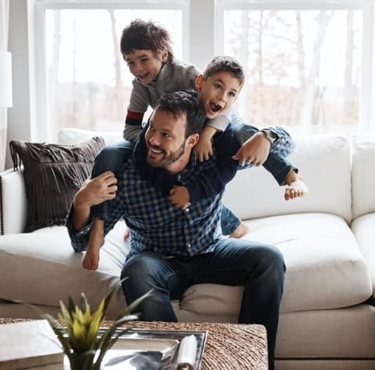 A man on a sofa playing with his three sons who are climbing on him