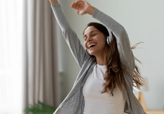A smiling woman dancing wearing headphones
